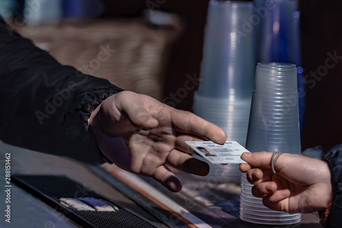 Canvas Print Young man show valid ID to buy alcohol and cigarettes in pub photographed with s