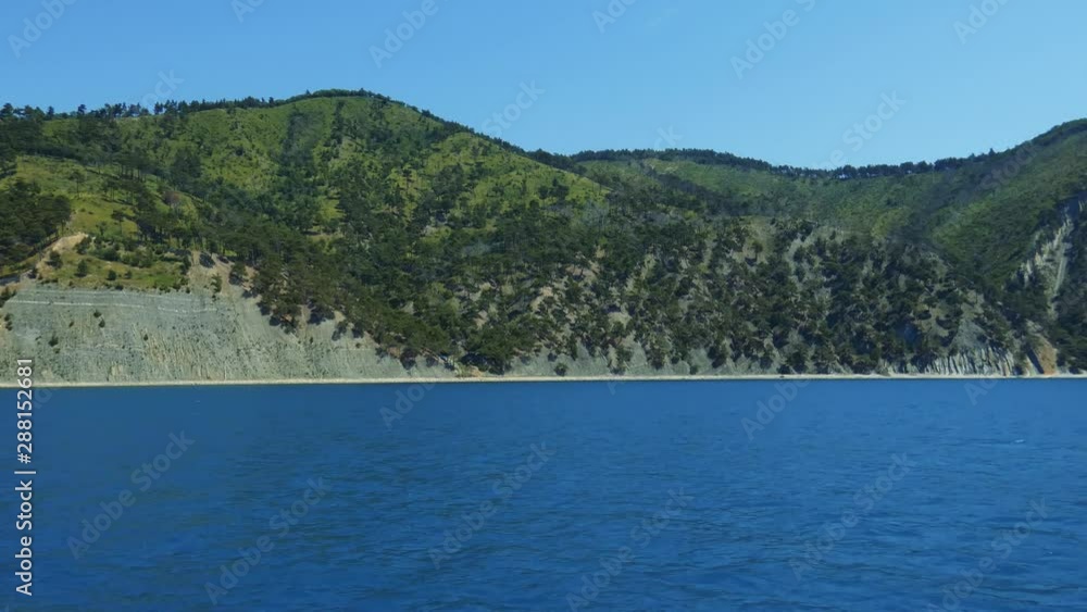 View from ship on sea coast. Blue water, small beach, big hills with forest. Summer sunny day. Black Sea, Russia. View from ship on sea coast. Blue water, small beach, big hills with forest. Summer sunny day. Black Sea, Russia.