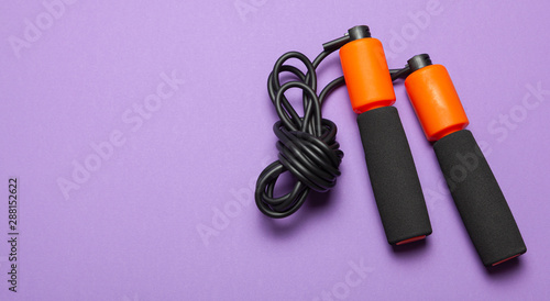 Jump rope. Fun exercises for body health. Orange rope with black cord. Violet background