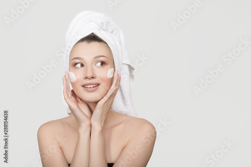 Portrait of a young woman with cream on her face. A towel around her head. White background