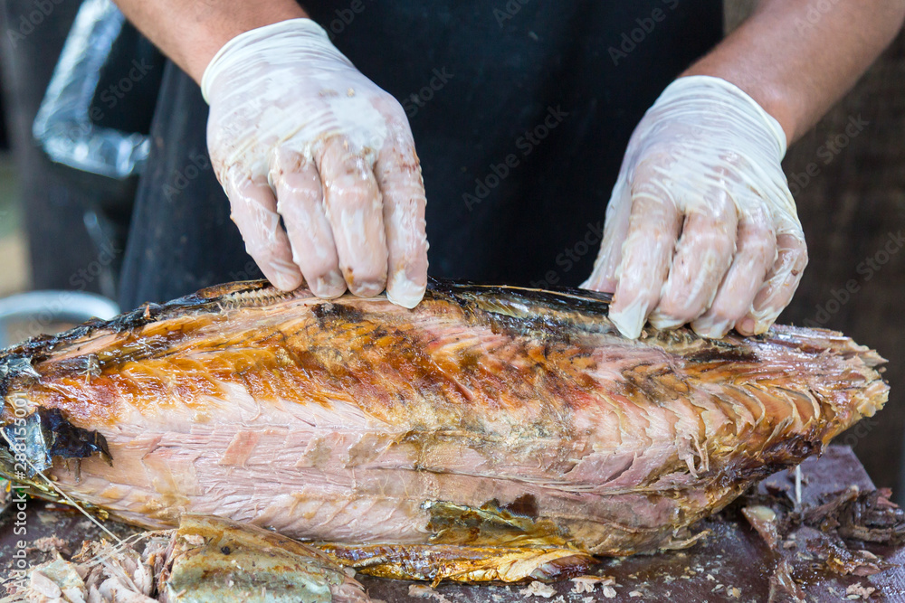 The cook is cutting large fried fish. Male hands in gloves break off pieces from a large fried fish.