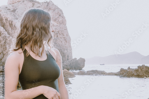 Sexy woman in black swimsuit, looking to the side the offer you can't miss. In front of the sea, traveler and adventurer looking for your next holiday destination. Travel concept.