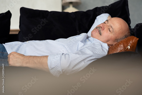 Tired senior hispanic man sleeping on dark blue couch, taking afternoon nap at the living room photo