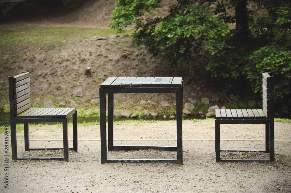 Chess table with two chairs on river bank on gloomy day Chess table with two chairs on river bank on gloomy day