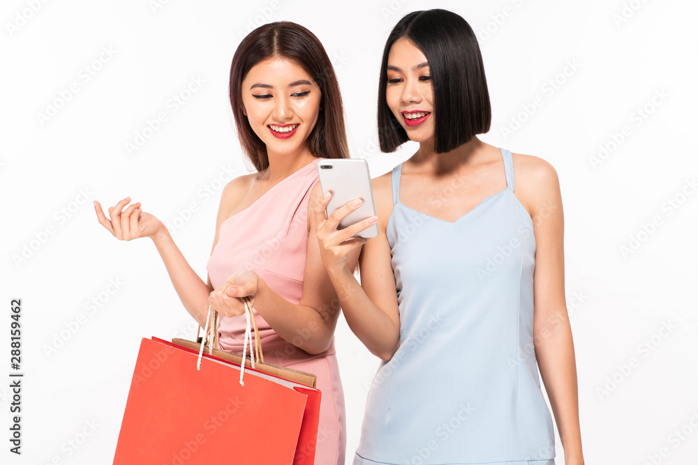 Shocked two women friends standing isolated over white background. Looking aside holding shopping bags using mobile phone Shocked two women friends standing isolated over white background. Looking aside holding shopping bags using mobile phone