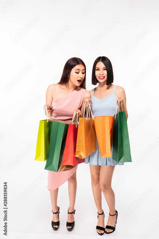 Excited happy young asia women friends posing isolated over white wall background holding shopping bags Excited happy young asia women friends posing isolated over white wall background holding shopping bags