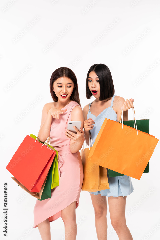 Excited happy young pretty women friends posing isolated over white wall background holding shopping bags Excited happy young pretty women friends posing isolated over white wall background holding shopping bags