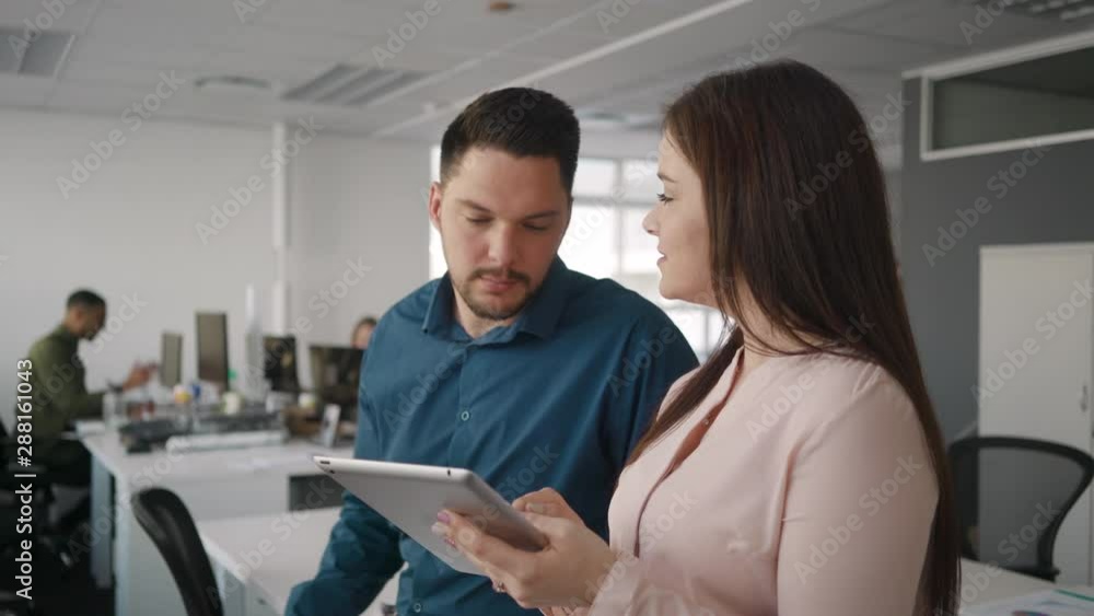 Professional young businessman and businesswoman discussing work together on digital tablet in modern office