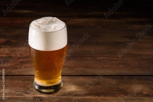 Glass of light beer on a dark pub. Glass beer on wood background with copy space. Full glass with lager beer, close up