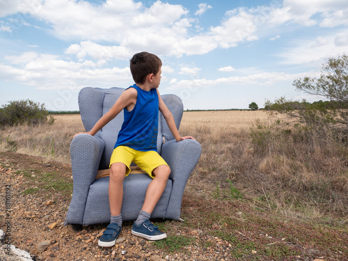 young boy sat on an old abandoned sofa in the middle of nowhere