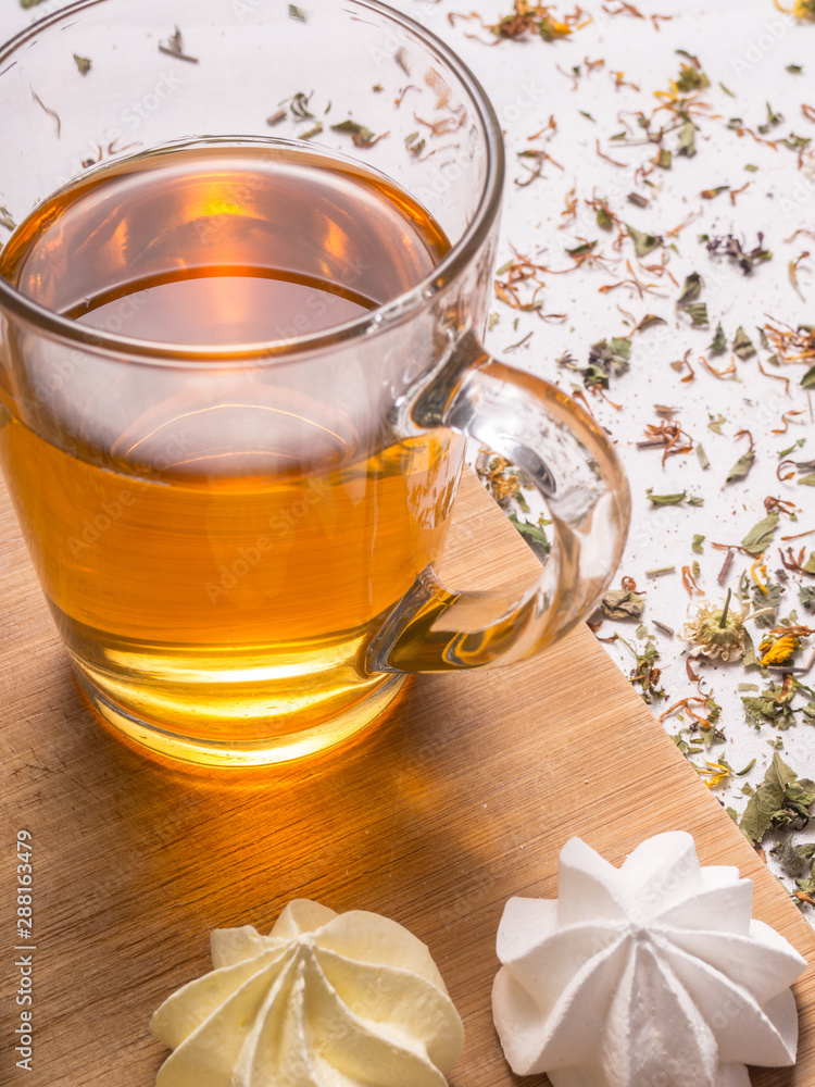 Closeup view of glass mug with hot herbal tea with crispy meringues and dried leaves and petals in the background Closeup view of glass mug with hot herbal tea with crispy meringues and dried leaves and petals in the background