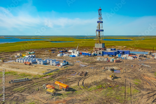 Drilling rig and equipment at an oil field in the northern tundra. Top view from a helicopter. Green summer tundra with lakes beyond the Arctic Circle.