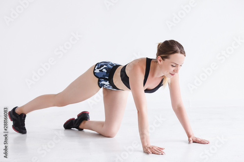 Sporty girl doing push-up exercises in gem with white wall. Attractive athletic woman doing basic exercises in fitness club. Fitness trainer texting new fitness program.