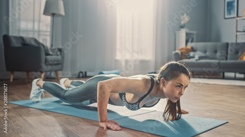 Strong Confident Beautiful Fitness Girl in Grey Athletic Sportswear is Doing Push Up Workout Exercises in Her Bright and Spacious Apartment with Cozy Minimalistic Interior.
