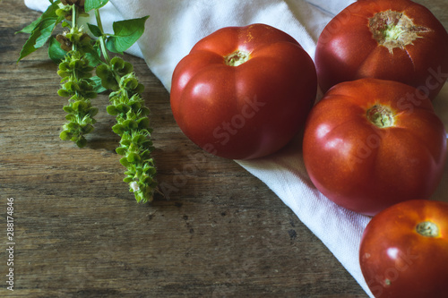 Fresh and tasty red tomatoes with basil on old wooden background