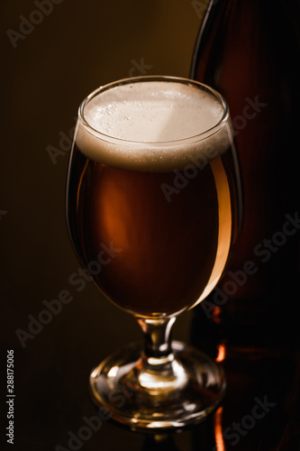 close up view of beer with white foam in glass on dark background with lighting