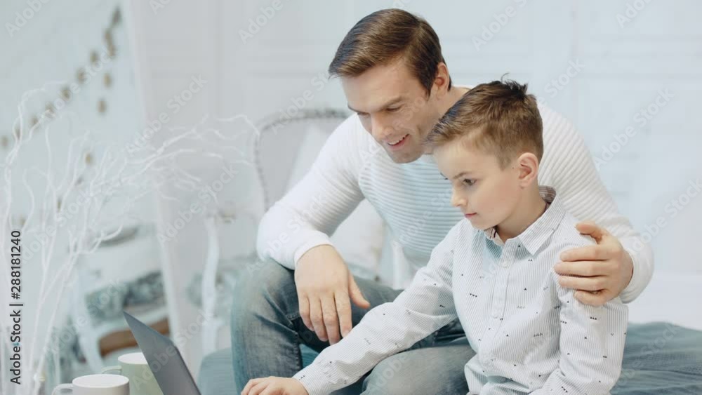 appy father hugging son looking computer screen in modern apartment. appy father hugging son looking computer screen in modern apartment.