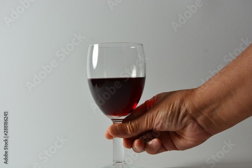 A person holding a glass of red wine in front of a white background