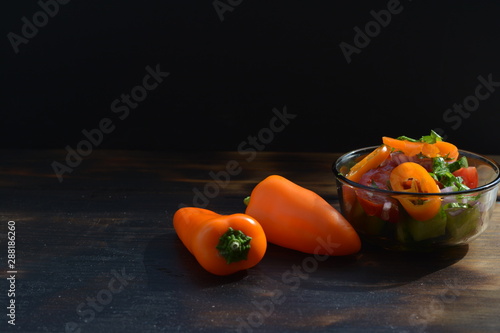 Orange peppers on a burned wooden table next to a small bowl of salad