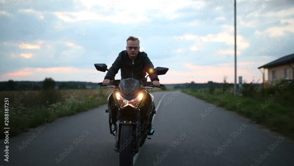 young man in a leather jacket with glasses rides a motorcycle on the road in the evening. young man in a leather jacket with glasses rides a motorcycle on the road in the evening.