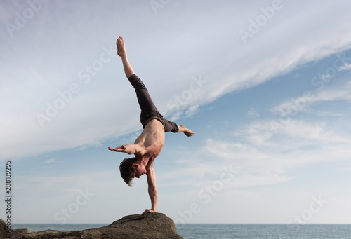 A young man performing a balancing act on the seashore. photo