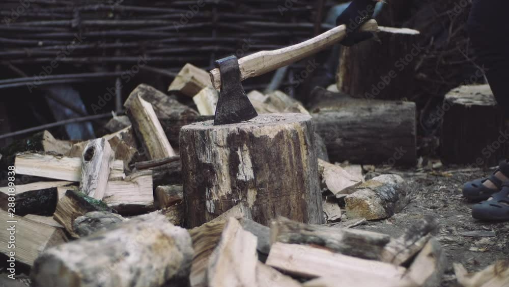 Man chops wood outdoors in slow motion. Man's hands working with ax. A man woodcutter chops tree trunks with an ax for firewood.