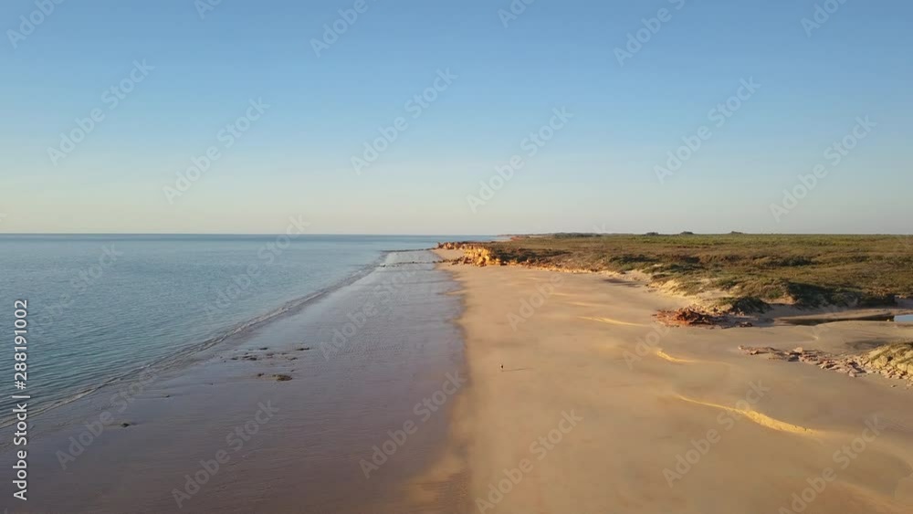 Aerial panoramic view of remote Kimberley coast in Western Australia, with single person walking along pristine ocean beach, steep rocky cliff and sunset blue sky as background. Aerial panoramic view of remote Kimberley coast in Western Australia, with single person walking along pristine ocean beach, steep rocky cliff and sunset blue sky as background.