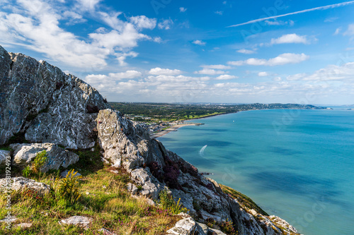 Summer Irish coastline landscape with tall and jagged cliffs in the foreground and a turquoise sea in the background. Colorful scenery from Bray Head, Wicklow, Ireland.