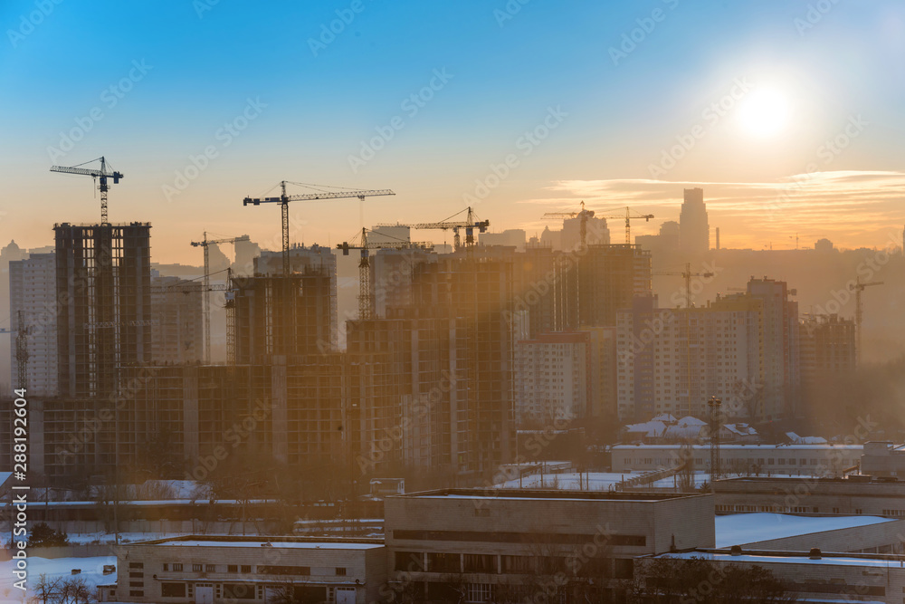 Panoramic view of sunset in the city with silhouette of buildings and industrial cranes Panoramic view of sunset in the city with silhouette of buildings and industrial cranes