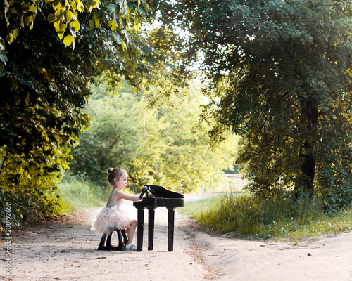 A little cute girl in an airy dress playing a piano in a summer green park. Outdoor 