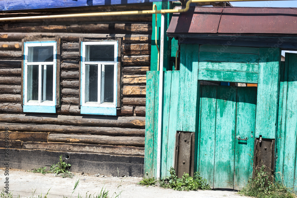 facade of an old log building with two windows and a green fence in a remote village facade of an old log building with two windows and a green fence in a remote village