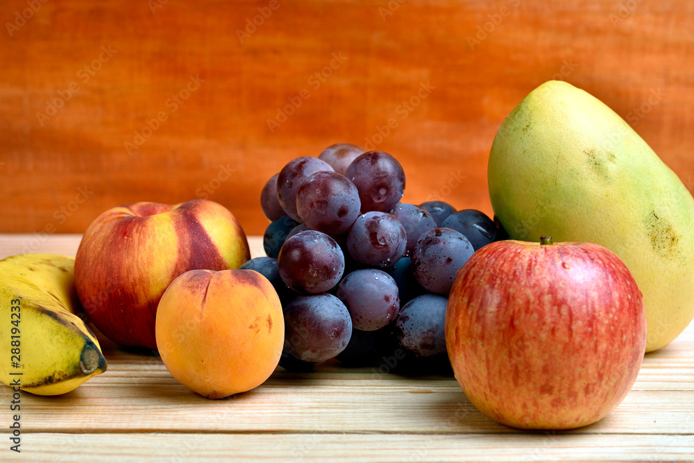 Seasonal fruits, peach, mango, apple, banana grapes, placed on a wooden base and diffuse background Seasonal fruits, peach, mango, apple, banana grapes, placed on a wooden base and diffuse background