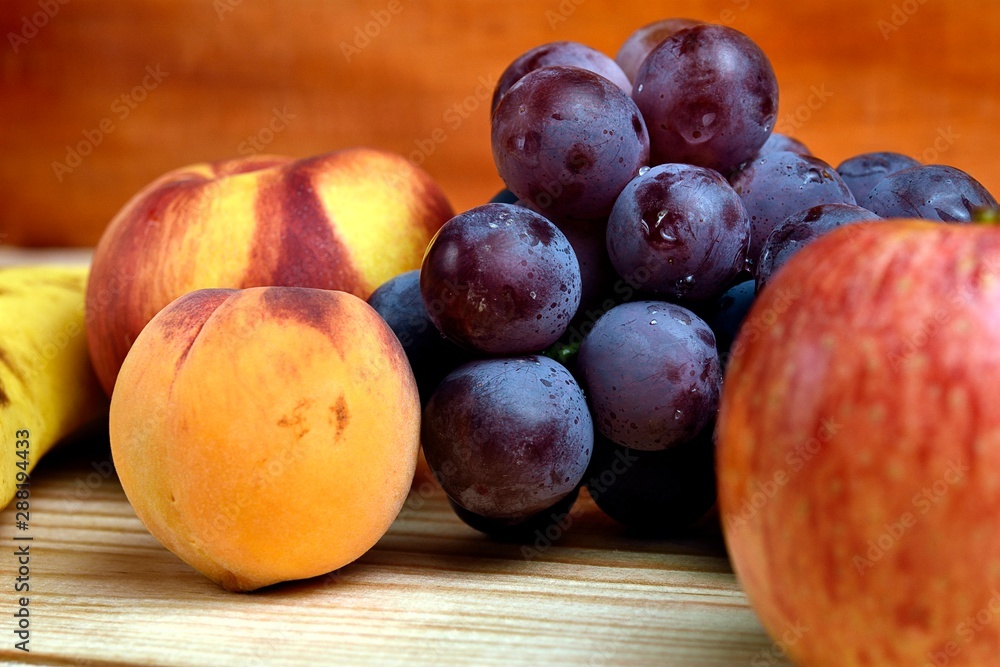 Seasonal fruits, peach, mango, apple, banana grapes, placed on a wooden base and diffuse background Seasonal fruits, peach, mango, apple, banana grapes, placed on a wooden base and diffuse background