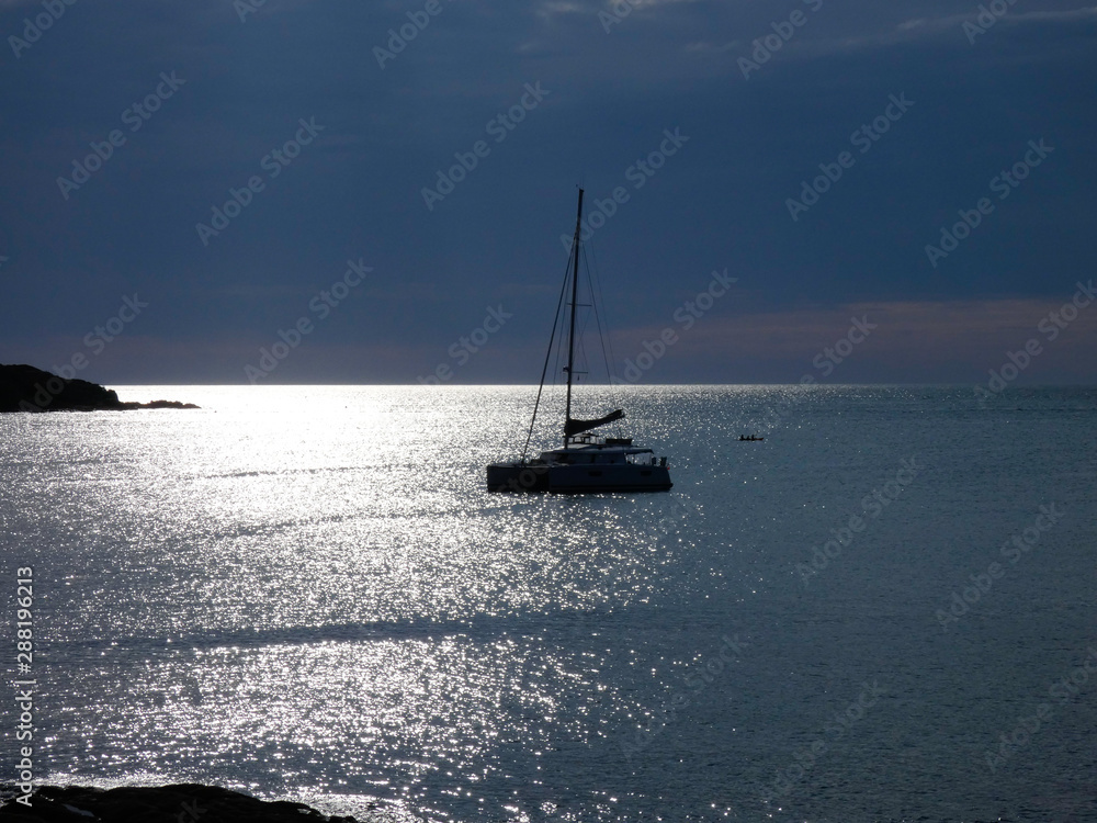 Obraz premium Barco velero anclado en el reflejo del sol en medio de una Bahía