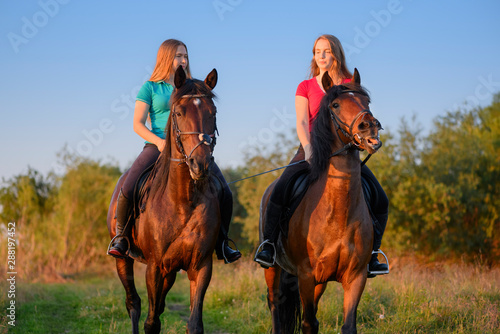 Two female teenagers are astride their bay horses in rural in sunset.