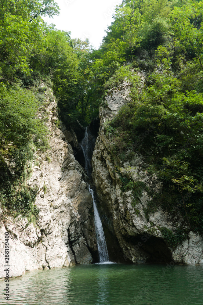 Waterfall in a crevice between the rocks behind the trees. Agur waterfalls in Sochi Waterfall in a crevice between the rocks behind the trees. Agur waterfalls in Sochi