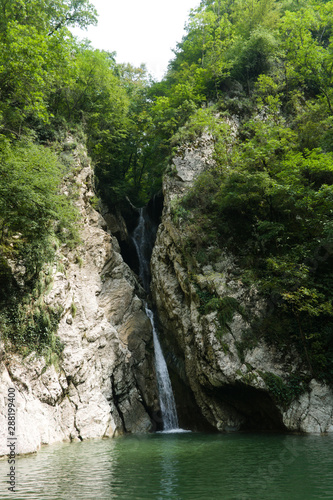 Waterfall in a crevice between the rocks behind the trees. Agur waterfalls in Sochi