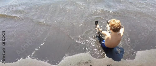 Little boy playing with black volcanic sand on the beach in Italy