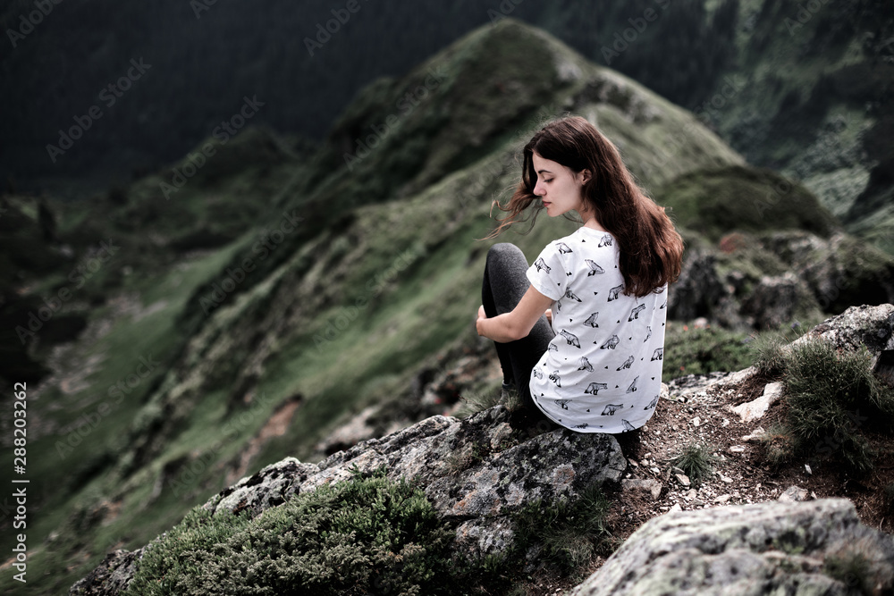 Rear view of a young woman sitting on a mountain top. Woman hiking around mountains