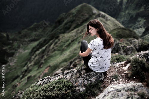 Rear view of a young woman sitting on a mountain top. Woman hiking around mountains