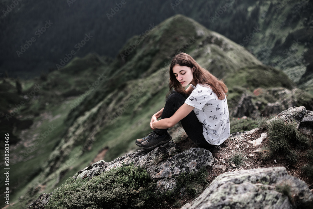 Young woman sitting on a mountain top. Woman hiking around mountains. Calm and inspiration on high peak of mountain