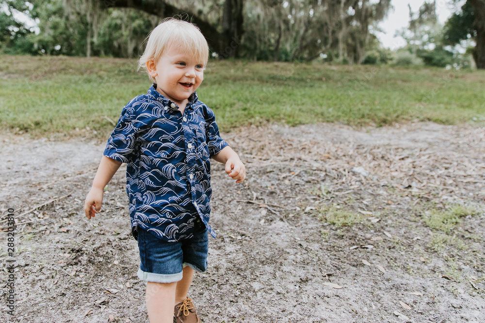 Adorably Happy and Cute Little Caucasian Toddler Baby Boy with Long Blond Hair Laughing, Playing, and Running Outside in Green Nature at the Park of Big Mature Oak and Moss Trees Adorably Happy and Cute Little Caucasian Toddler Baby Boy with Long Blond Hair Laughing, Playing, and Running Outside in Green Nature at the Park of Big Mature Oak and Moss Trees