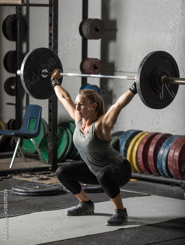 Fototapeta Naklejka Na Ścianę i Meble -  Young, strong, female weight lifter practicing snatch in weight room with heavy barbell.