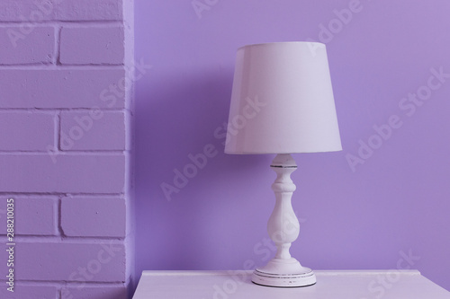 White table lamp stands on a white nightstand against a lilac wall