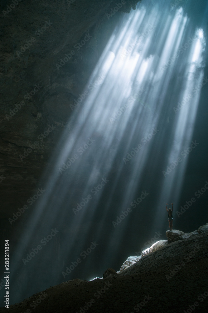 Foto de Girl stands under the rays of light in a deep cave Jomblang ...