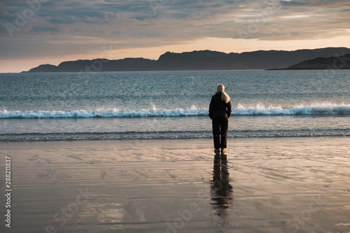 A girl stands on the shore of the Barents Sea at sunrise