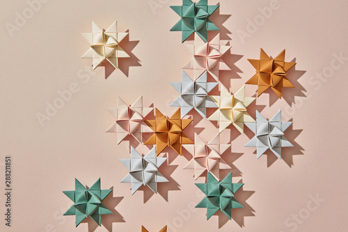 Handcraft colorful origami stars on a light brown background with reflection of shadows and copy space. Flat lay