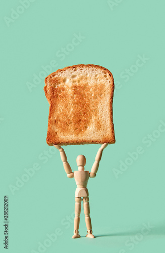 Miniature articulation mannequin holds fresh toast in his hand on a green background, copy space.