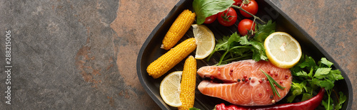 top view of raw salmon steak with vegetables, lemon and herbs in grill pan, panoramic shot