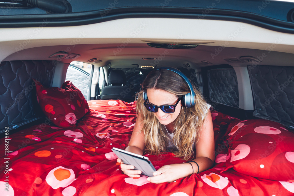 Pretty blonde woman with sunglasses and headphones in camping inside a van  using tablet Stock-foto | Adobe Stock